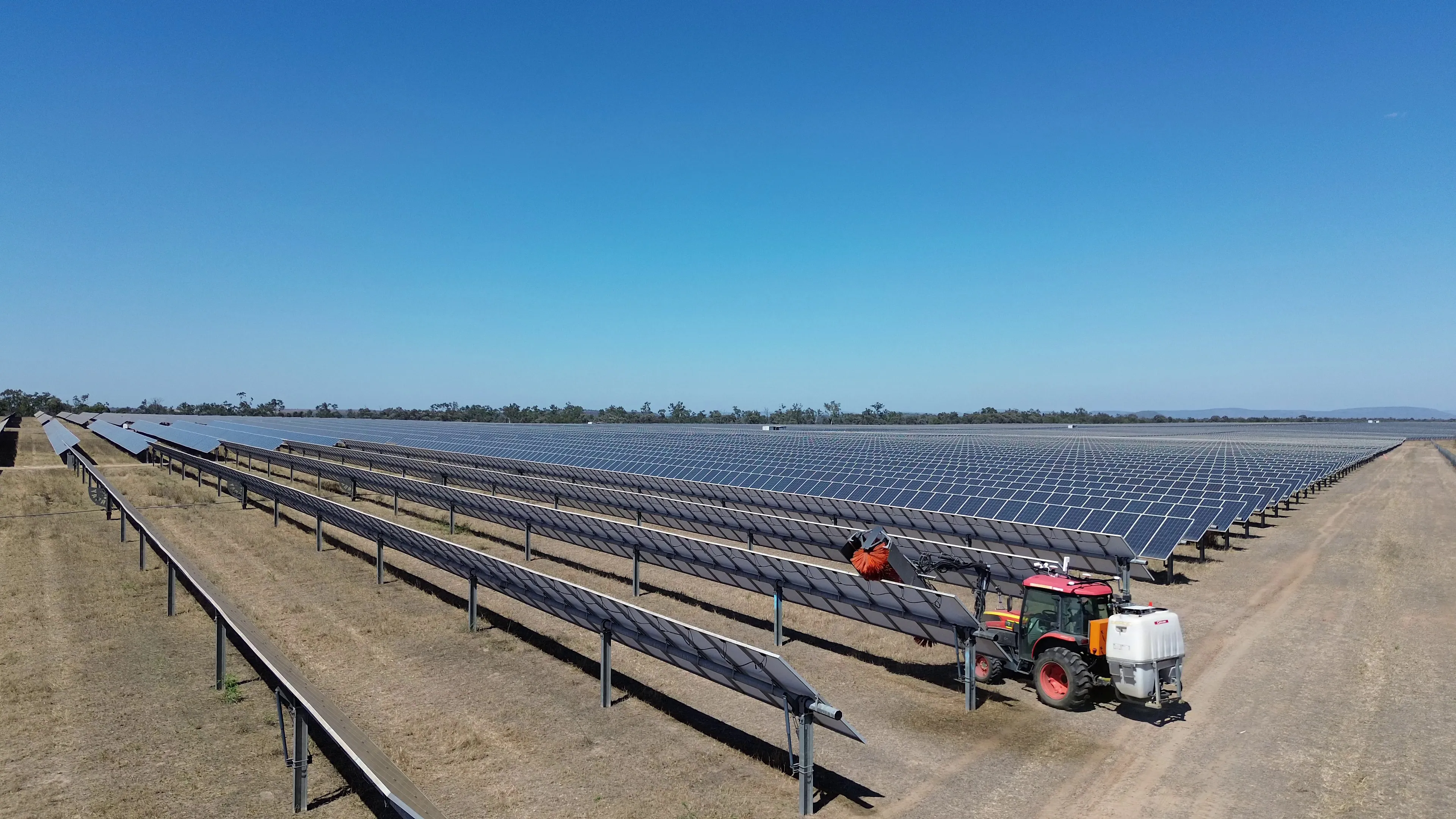 The ARC1 autonomous cleaning platform working a row at a utility-scale solar farm that stretches to the horizon